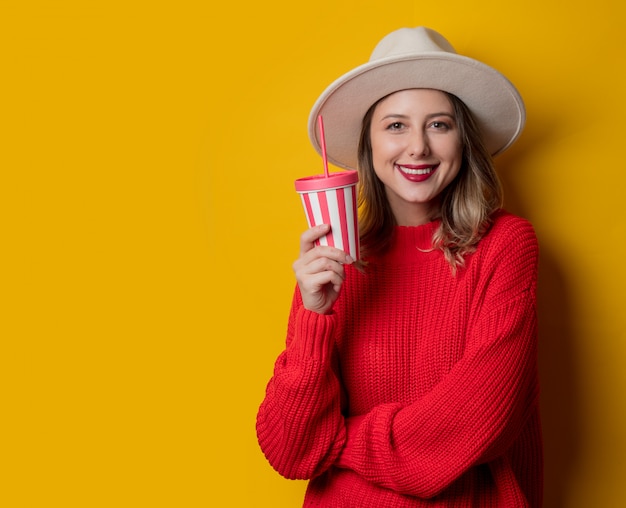 Femme au chapeau et pull rouge avec boisson