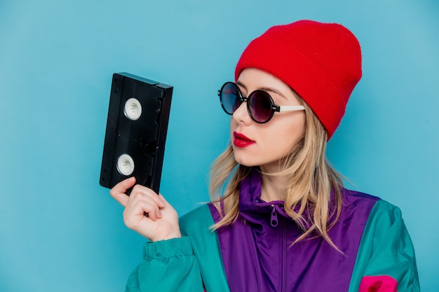 femme au chapeau rouge, lunettes de soleil et costume des années 90 avec cassette VHS