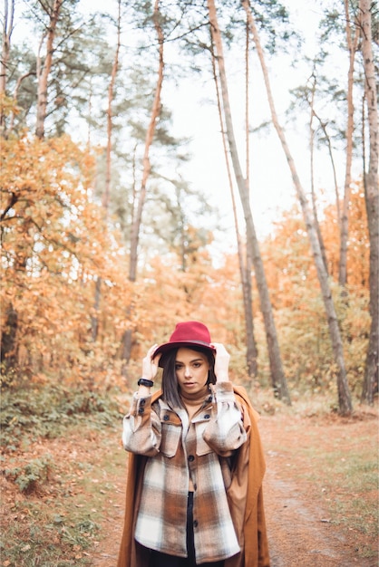 Une femme au chapeau rouge se tient dans les bois en automne.