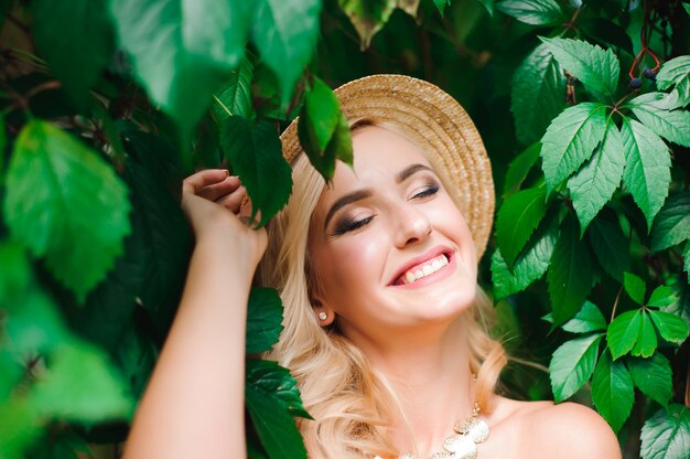 Femme au chapeau et vêtements d'été posant près des feuilles vertes