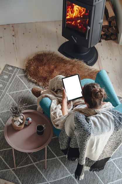 Femme au coin du feu, assise dans un fauteuil confortable, avec une ambiance chaleureuse