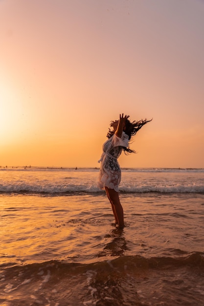 Une femme au coucher du soleil dans une robe blanche dans la mer en été jetant de l'eau