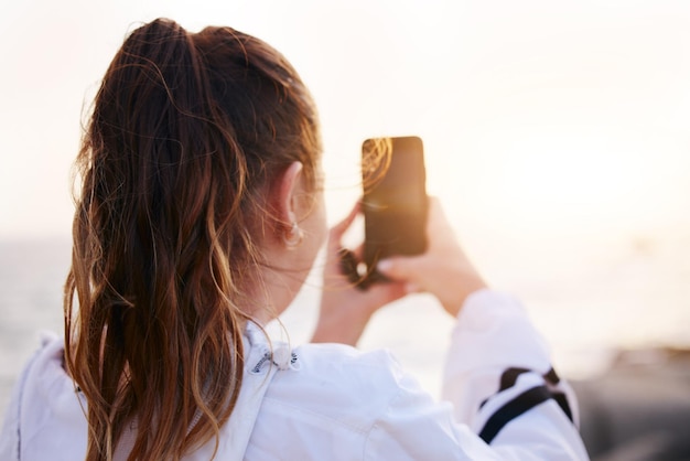 Femme au dos ou au téléphone photo du coucher de soleil sur la plage au bord de l'océan ou de la mer dans l'environnement naturel vacances vacances ou lieu de voyage au Canada Touriste étudiant ou influenceur sur la technologie de photographie mobile ou vlog