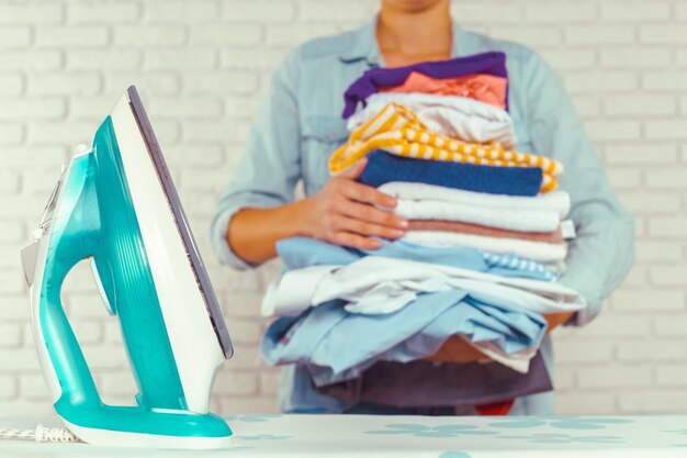 Photo femme au foyer apportant un énorme tas de linge sur la planche à repasser