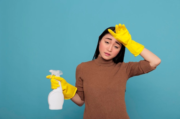 Femme au foyer asiatique fatiguée, frustrée et malheureuse de tout le nettoyage portant des gants en caoutchouc jaune. Femme de ménage surmenée stressée épuisée par les travaux ménagers et les tâches ménagères avec un état d'esprit négatif