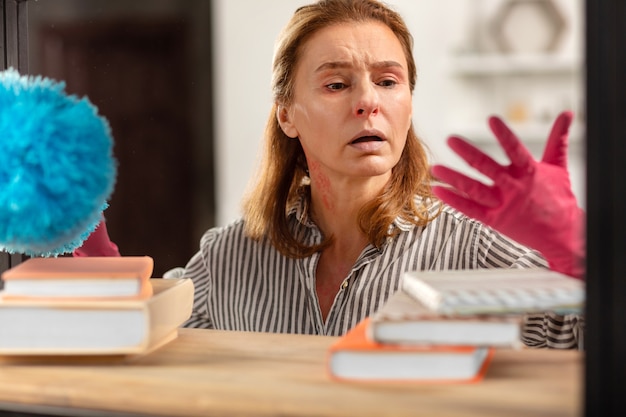 Femme au foyer aux yeux noirs portant des gants roses se sentant fatiguée de la poussière tout en ayant une allergie