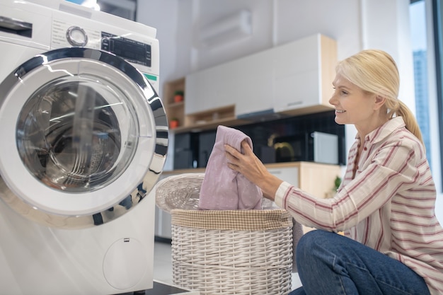 Femme au foyer blonde mettre des vêtements dans une machine à laver