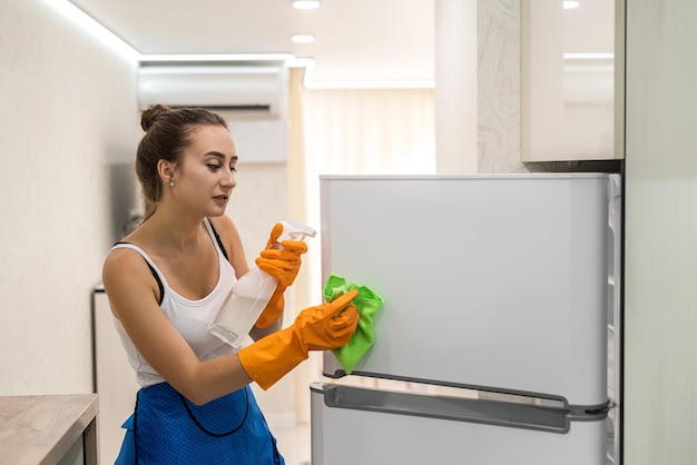 Une femme au foyer caucasienne nettoie avec un spray et des gants de protection la cuisine chez elle