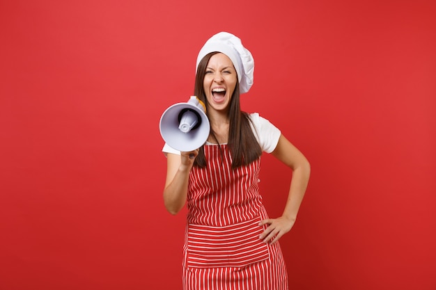 Femme au foyer chef cuisinier ou boulanger en tablier rayé, t-shirt blanc, chapeau de chef toque isolé sur fond de mur rouge. Une femme crie dans un mégaphone, annonce la vente de rabais. Maquette du concept d'espace de copie.