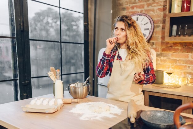 Femme au foyer contre table avec de la farine, des œufs et du lait