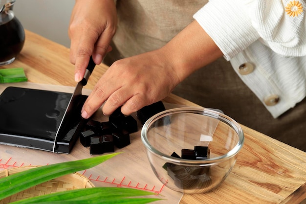 Femme au foyer coupe Cincau Hitam ou Pudding de gelée d'herbe noire en morceaux d'aliments sains