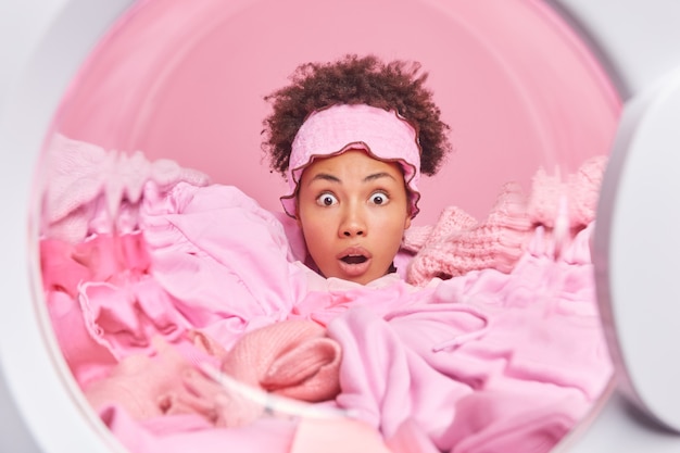 Photo une femme au foyer étonnée passe la tête à travers le linge dans la machine à laver regarde les yeux obsédés réagit aux nouvelles choquantes a beaucoup de tâches ménagères à l'intérieur de la machine à laver