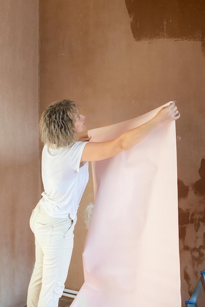 une femme au foyer fait indépendamment des réparations dans son appartement colle du papier peint sur les murs