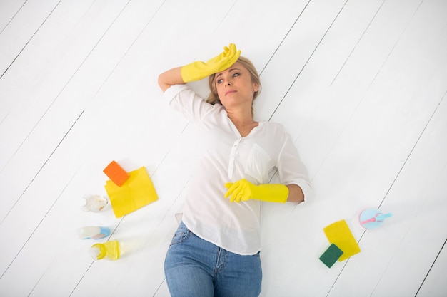 Femme au foyer fatiguée dans des gants jaunes portant sur le sol