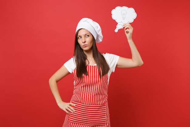 Femme au foyer femme chef cuisinier ou boulanger en tablier rayé t-shirt blanc toque chapeau de chef isolé sur fond de mur rouge. Une femme pensive pense, tiens le nuage avec une idée d'ampoule. Maquette du concept d'espace de copie.