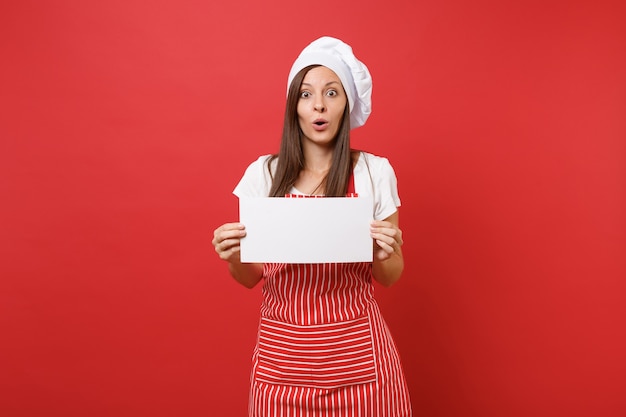 Femme au foyer femme chef cuisinier ou boulanger en tablier rayé t-shirt blanc toque chapeau de chef isolé sur fond de mur rouge. Une femme tient un panneau vierge, place pour le texte promotionnel. Maquette du concept d'espace de copie.