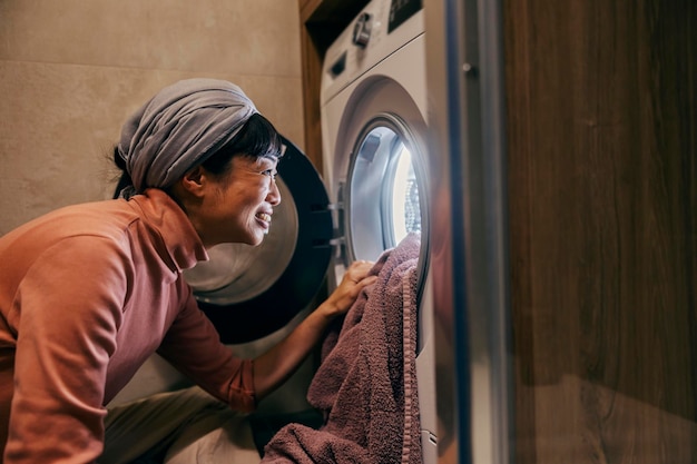 Une femme au foyer japonaise heureuse met du linge dans une machine à laver dans la salle de bain.