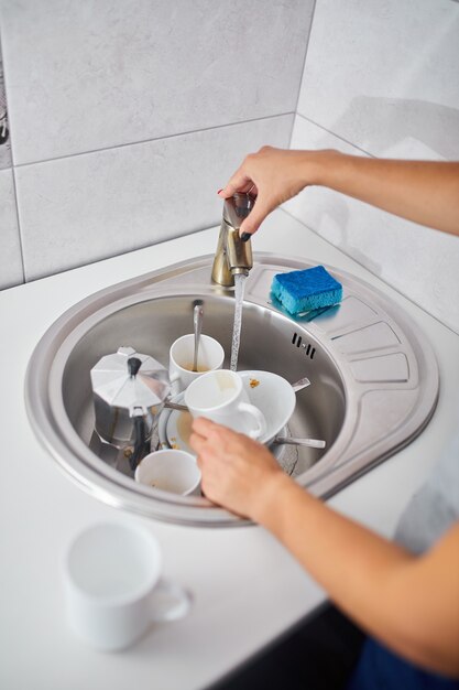 Femme au foyer méconnaissable lavant la vaisselle dans la cuisine à la maison au-dessus de l'évier, mode de vie, équipement de la maison.