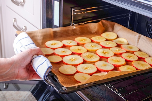 Une femme au foyer met une plaque de cuisson de pommes tranchées dans un four électrique pour sécher. Fruits secs, nourriture saine. Orientation horizontale, mise au point sélective.