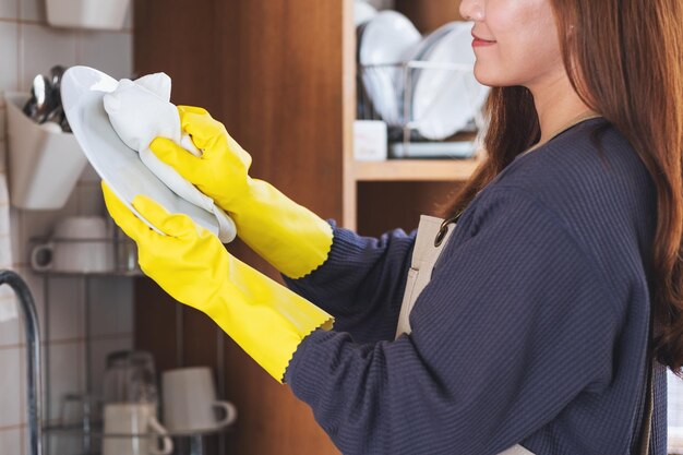 Une femme au foyer portant un tablier et un gant de protection nettoyant et lavant la vaisselle dans la cuisine à la maison