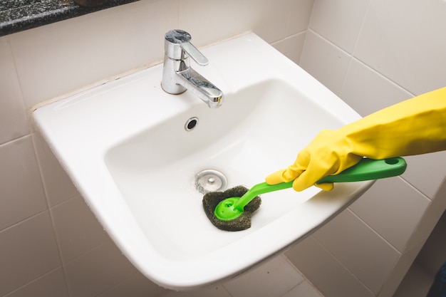 Femme au foyer porte un gant de caoutchouc jaune et à l&#39;aide de la brosse de nettoyage du bassin sale dans les toilettes