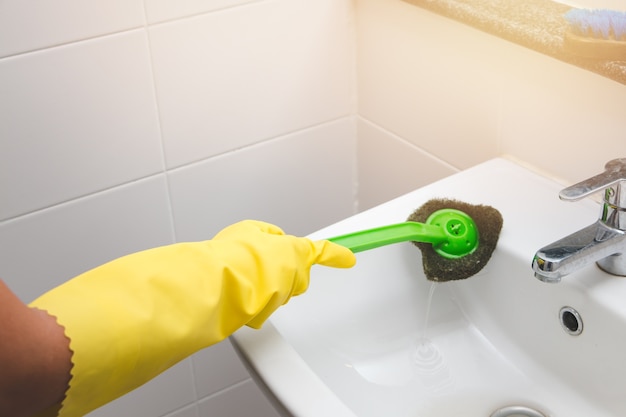 Femme au foyer porte un gant de caoutchouc jaune et à l&#39;aide de la brosse de nettoyage du bassin sale dans les toilettes