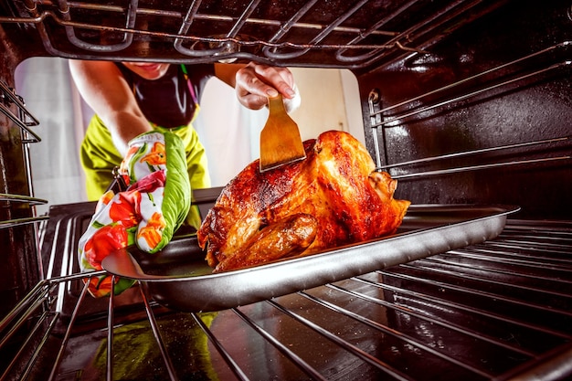 La femme au foyer prépare le poulet rôti au four, vue depuis l'intérieur du four. Cuisson au four.