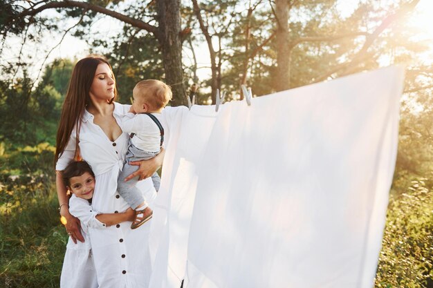 Femme au foyer séchant les vêtements Jeune mère avec sa petite fille et son fils est à l'extérieur dans la forêt Beau soleil