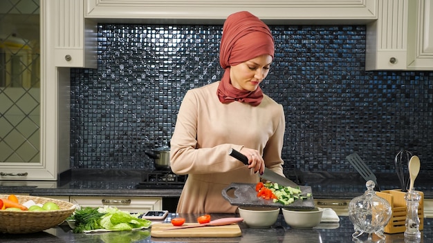 Une femme au foyer séduisante en hijab a mis des légumes frais coupés dans des assiettes creuses préparant de la nourriture halal pour le mari en gros plan