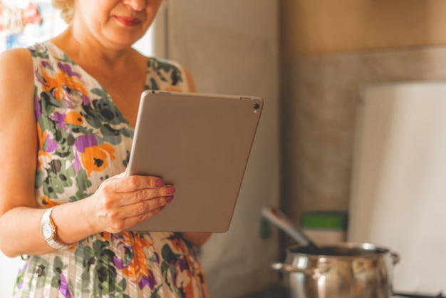 Femme au foyer tenant un smartphone ou une tablette gadget pour vérifier le reçu pendant la cuisson à la cuisine