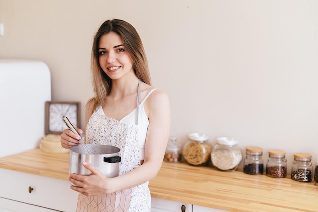 Une femme au foyer tient une casserole et un fouet dans ses mains Une fille dans un tablier se tient dans la cuisine