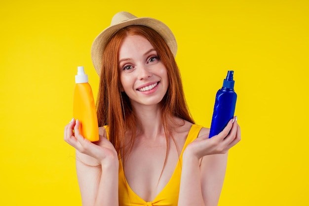 Femme au gingembre rousse en soutien-gorge élégant tenant une bouteille en plastique de lotion spf sur fond jaune studio.