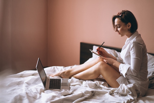 Femme au lit avec des affaires informatiques