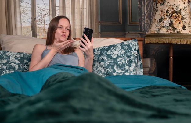 Femme au lit lors d'un appel vidéo par téléphone portable envoyant un baiser aérien au smartphone