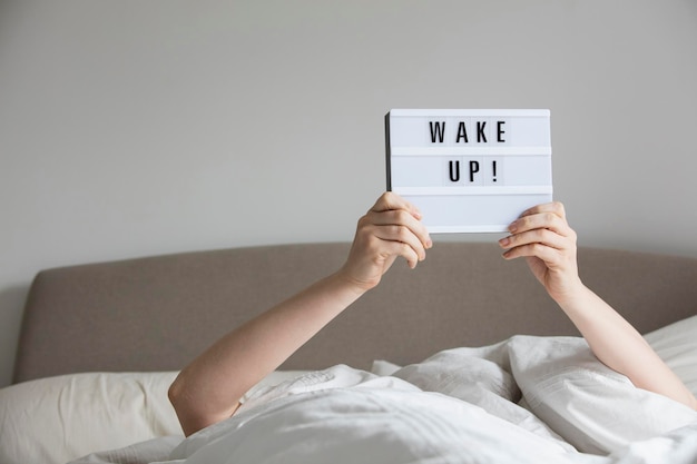 Femme au lit sous les draps tenant un panneau de réveil