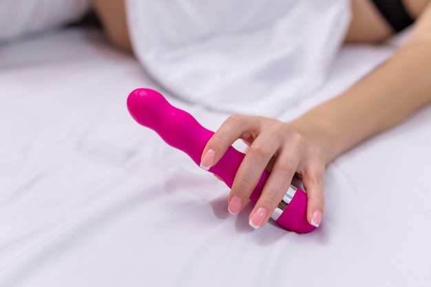 Femme au lit sous des draps tenant un vibromasseur à la main