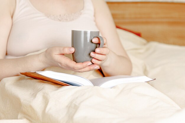 Femme au lit avec une tasse de thé et un livre. Femme adulte lisant dans le lit.