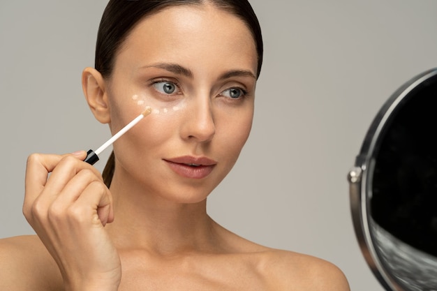 Femme au maquillage naturel appliquant un correcteur sur une peau fraîche impeccable