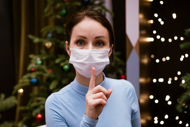 Femme au masque médical montre le geste du doigt pour être calme sur fond de bokeh