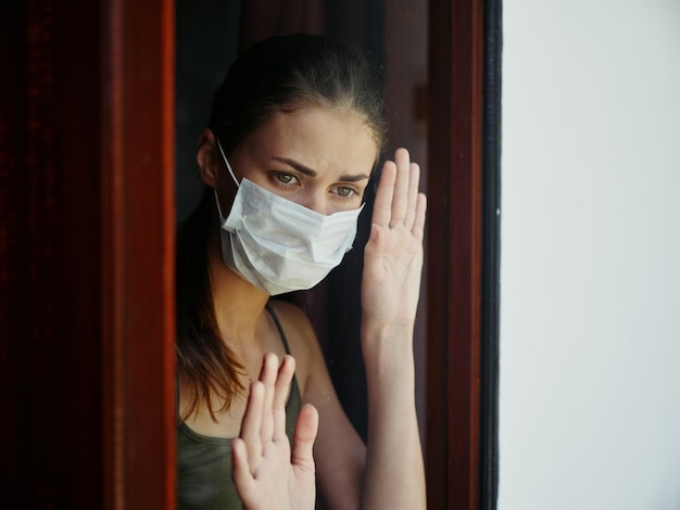 Femme au masque médical regard triste depuis l'interdiction de la fenêtre