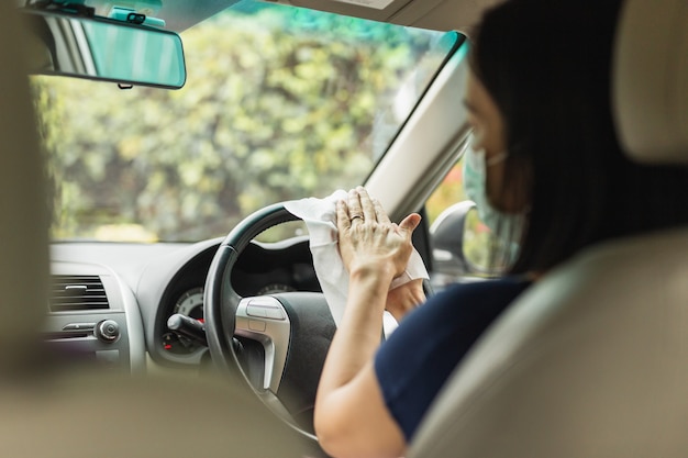 Femme au masque médical se nettoyant les mains avec des lingettes humides alors qu'elle était assise dans sa voiture