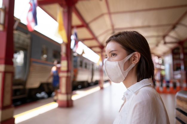 Femme au masque de protection attendre le train local sur la plate-forme à la gare.