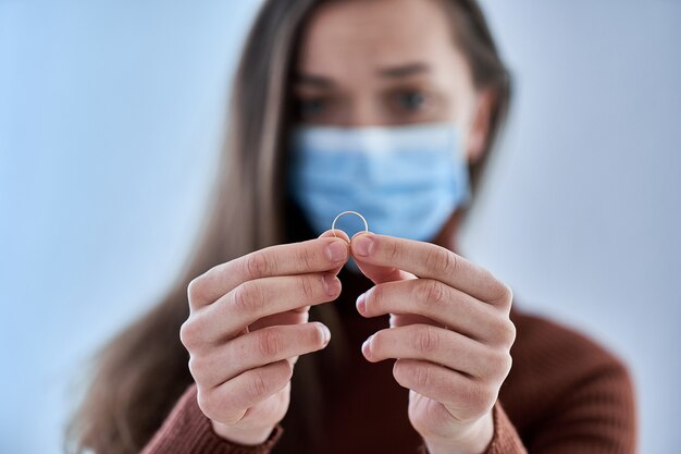 Femme au masque de protection détient l'anneau. Rompre la relation après avoir vécu ensemble et rester à la maison pendant la quarantaine et l'isolement en raison de l'épidémie de coronavirus. Concept de divorce