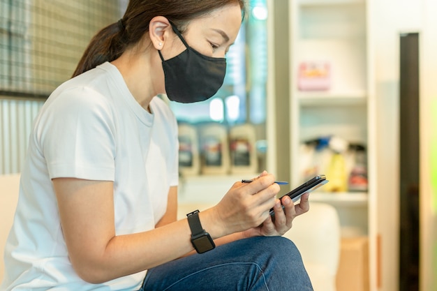 Femme au masque de protection travaillant sur un téléphone intelligent à l'aide d'un stylo numérique.