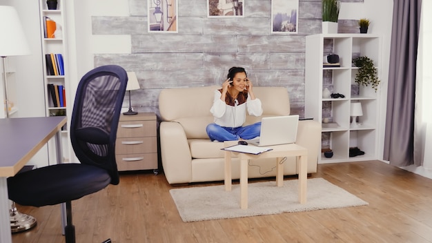 Femme au ralenti mettant des écouteurs lors d'un appel vidéo tout en travaillant à domicile.