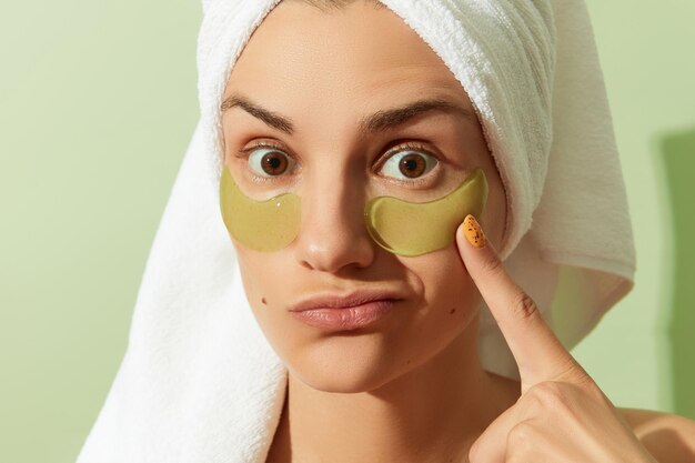 Femme au soleil avec des pansements oculaires sur fond vert pastel routine de soins de la peau du matin