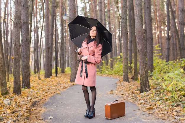 Femme en automne parc marchant avec valise rétro et parapluie