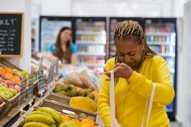 Femme aux cheveux afro mettant des fruits dans le sac écologique