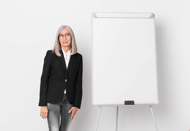 Femme aux cheveux blancs d'âge moyen se sentant triste, contrariée ou en colère et regardant sur le côté et un espace de copie de planche. concept d'entreprise