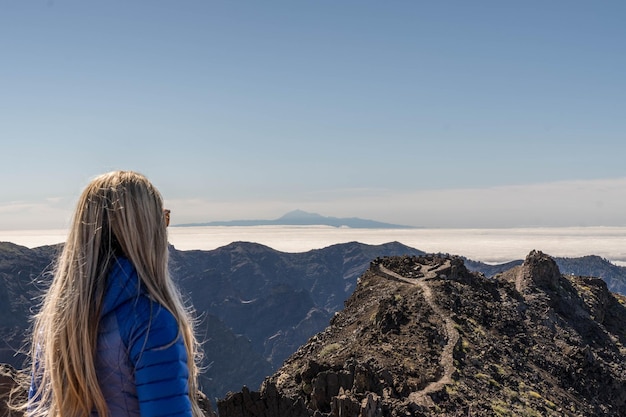 Femme aux cheveux blonds au sommet de la montagne avec une veste bleue